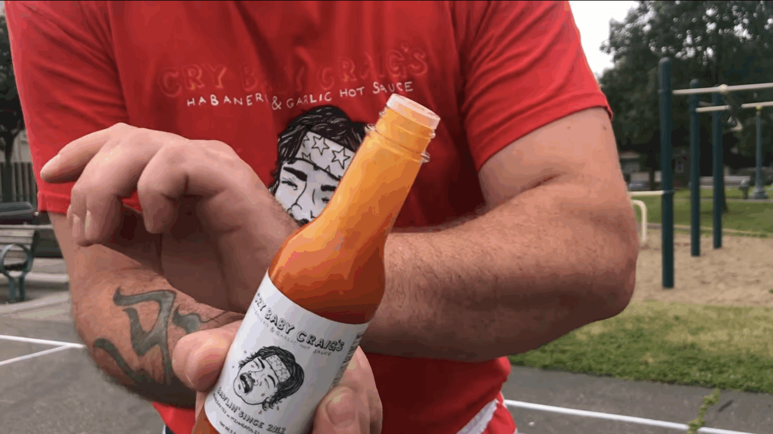 Close-up of Cry Baby Craig’s Habanero & Garlic Hot Sauce bottle being held outdoors.