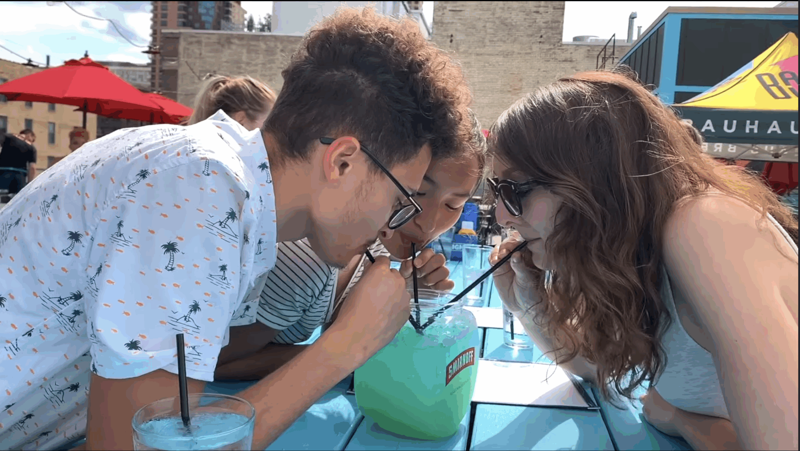Three people sharing a large blue cocktail outdoors at a Madison Restaurant Group restaurant patio.